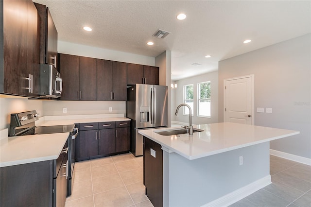 kitchen featuring sink, stainless steel appliances, an island with sink, light tile patterned floors, and dark brown cabinetry