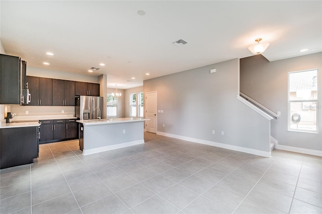 kitchen featuring stainless steel appliances, a center island with sink, light tile patterned floors, and dark brown cabinetry