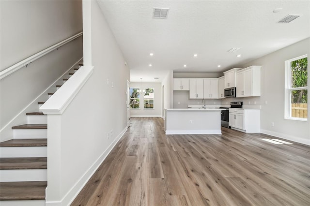 2909 W Spruce St, Tampa, FL 33607 - kitchen featuring appliances with stainless steel finishes, light wood-style floors, white cabinets, an island with sink, and light countertops