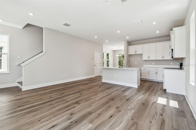 2909 W Spruce St, Tampa, FL 33607 - kitchen with light wood-style flooring, white cabinets, a center island with sink, open floor plan, and stainless steel microwave