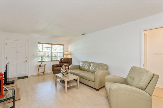 living area featuring baseboards, visible vents, a textured ceiling, and light wood finished floors