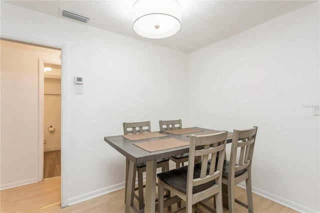 dining area with light wood-type flooring, visible vents, and baseboards