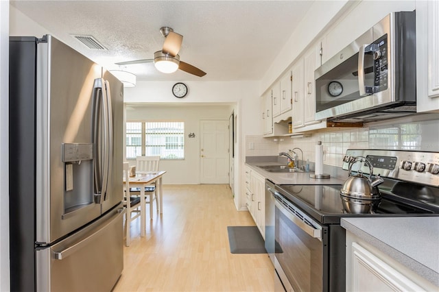 kitchen featuring stainless steel appliances, a sink, visible vents, white cabinets, and backsplash