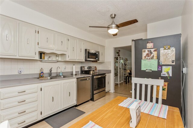 kitchen featuring light wood finished floors, tasteful backsplash, appliances with stainless steel finishes, a ceiling fan, and a sink