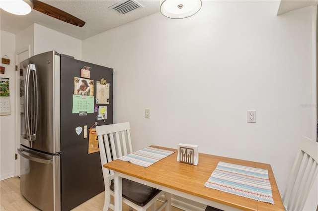 dining area featuring light wood-type flooring, ceiling fan, visible vents, and a textured ceiling