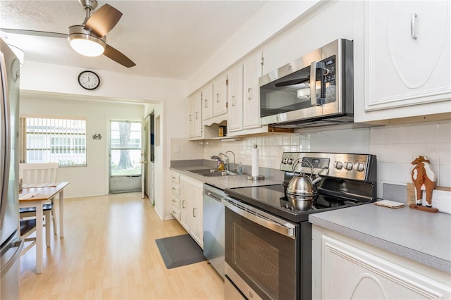 kitchen with tasteful backsplash, appliances with stainless steel finishes, light wood-style floors, white cabinets, and a sink