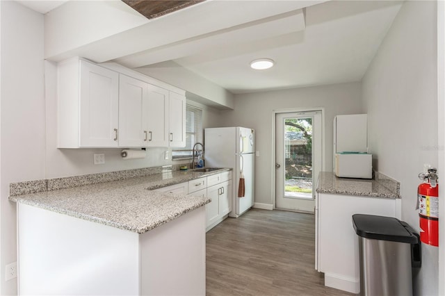 kitchen with a peninsula, white appliances, a sink, white cabinetry, and light wood-type flooring