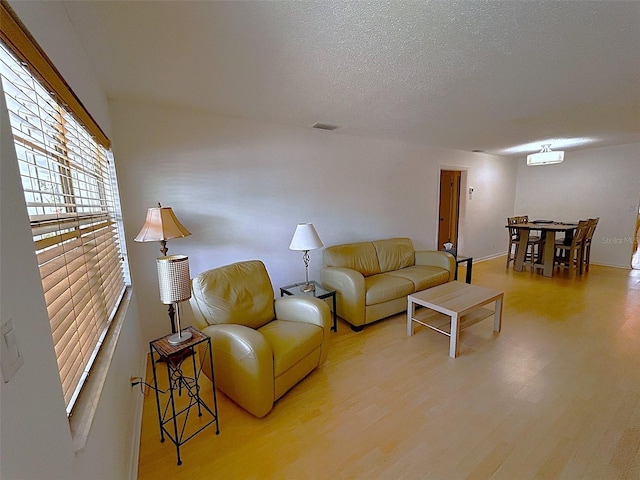 living room with a textured ceiling, light wood-type flooring, and visible vents