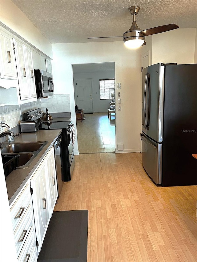 kitchen with dark countertops, appliances with stainless steel finishes, light wood-type flooring, white cabinetry, and a sink