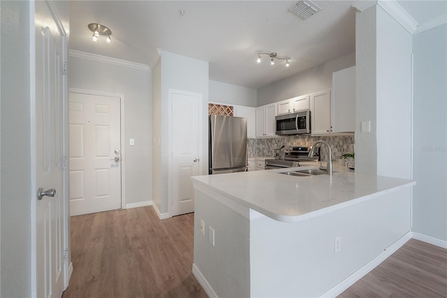 kitchen with sink, backsplash, kitchen peninsula, white cabinets, and appliances with stainless steel finishes