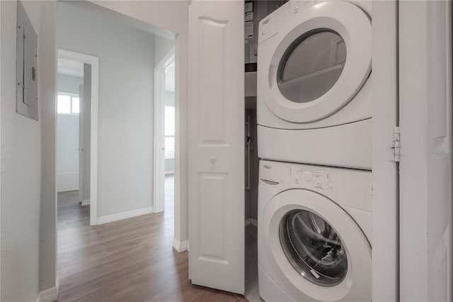 laundry area with electric panel, wood-type flooring, and stacked washer / drying machine