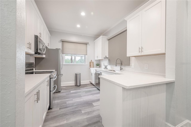 kitchen with kitchen peninsula, appliances with stainless steel finishes, ornamental molding, sink, and white cabinets