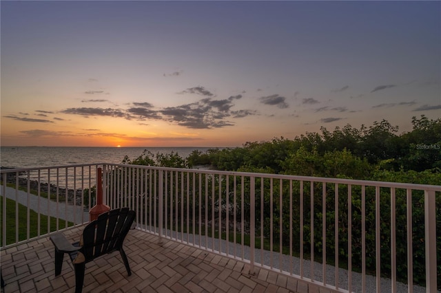 balcony at dusk featuring a water view