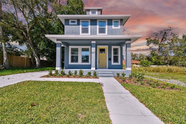 traditional style home featuring stucco siding, covered porch, a front yard, and fence