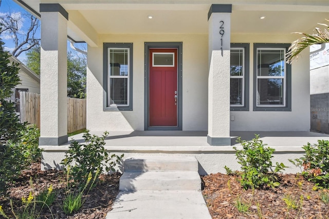 property entrance with covered porch, fence, and stucco siding