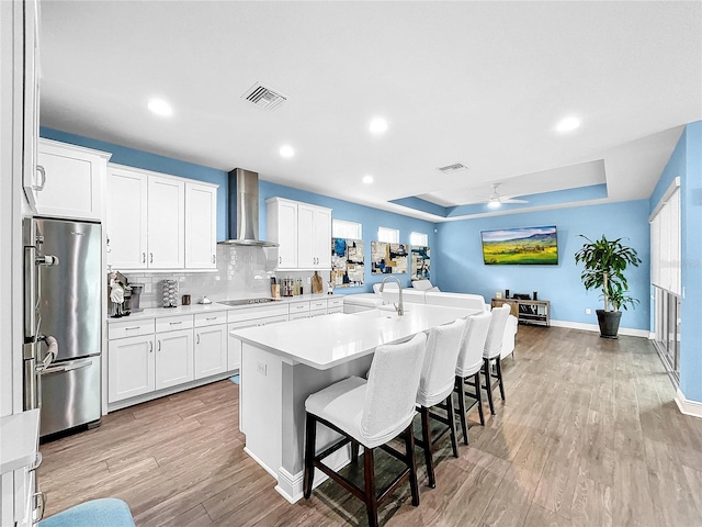 kitchen with white cabinetry, stainless steel fridge, a center island with sink, and wall chimney exhaust hood