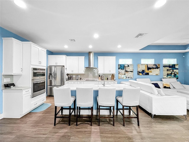 kitchen with white cabinets, a kitchen breakfast bar, wall chimney range hood, and appliances with stainless steel finishes