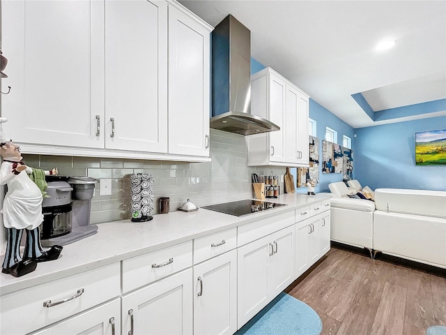 kitchen with white cabinetry, wall chimney range hood, tasteful backsplash, black electric stovetop, and light wood-type flooring