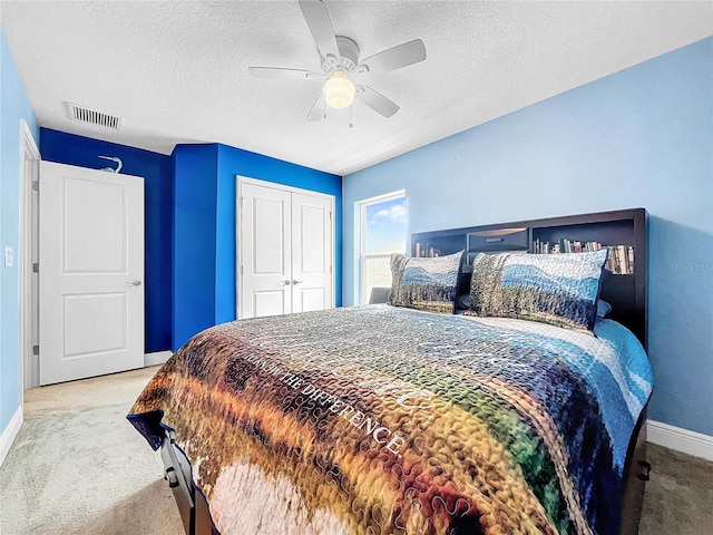 bedroom with a textured ceiling, ceiling fan, light carpet, and a closet