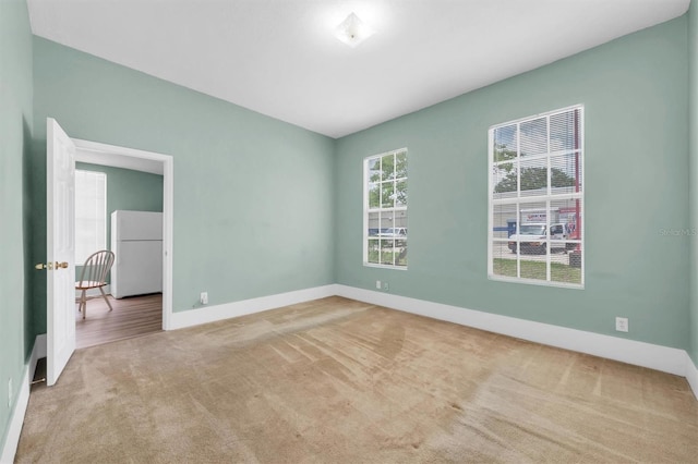 spare room featuring light carpet and baseboards