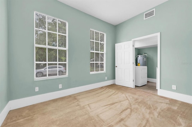 empty room featuring visible vents, light carpet, baseboards, and water heater