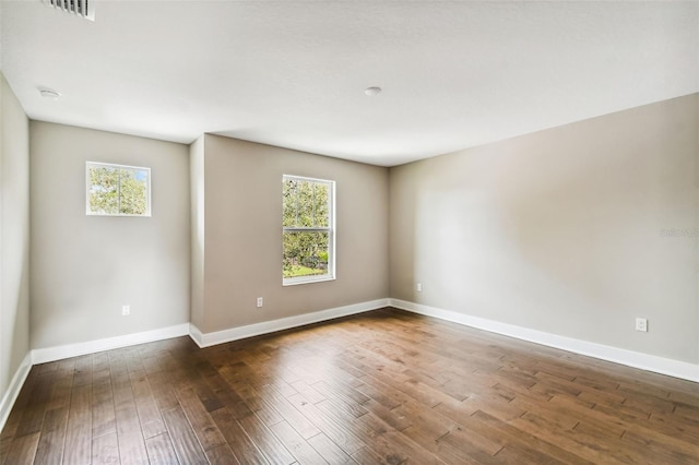 unfurnished room with plenty of natural light, visible vents, baseboards, and dark wood-type flooring