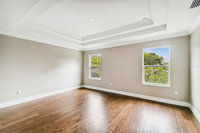 empty room featuring a tray ceiling, visible vents, baseboards, and wood finished floors