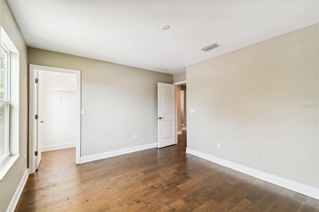 unfurnished bedroom with wood finished floors, visible vents, baseboards, a closet, and a walk in closet