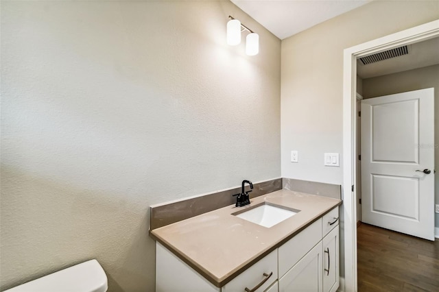 half bath featuring toilet, vanity, wood finished floors, and visible vents