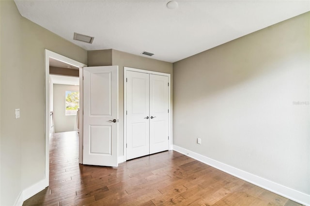 unfurnished bedroom with a closet, wood finished floors, visible vents, and baseboards