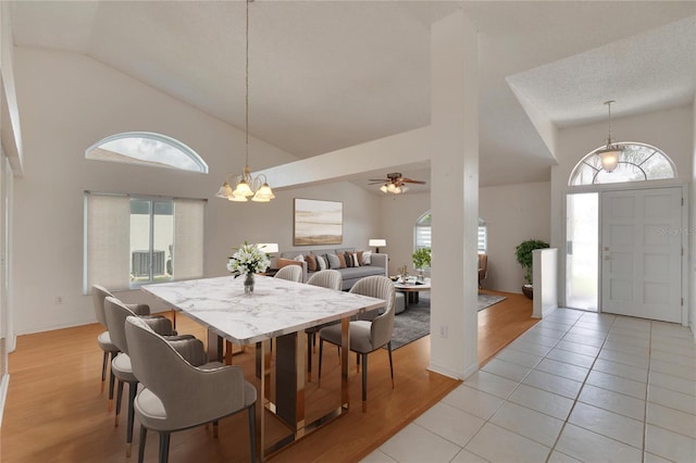 dining space with ceiling fan with notable chandelier, light wood-type flooring, a textured ceiling, and high vaulted ceiling