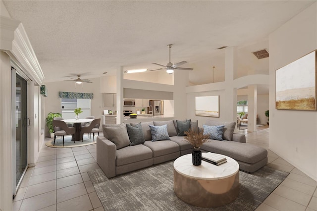 tiled living room with ceiling fan, a textured ceiling, and high vaulted ceiling