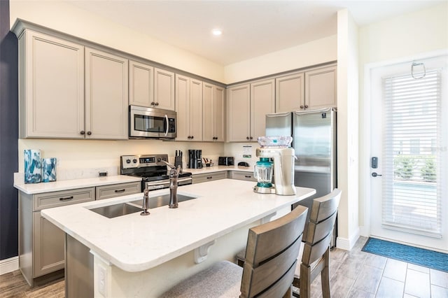 kitchen featuring a kitchen breakfast bar, gray cabinets, a center island with sink, and stainless steel appliances