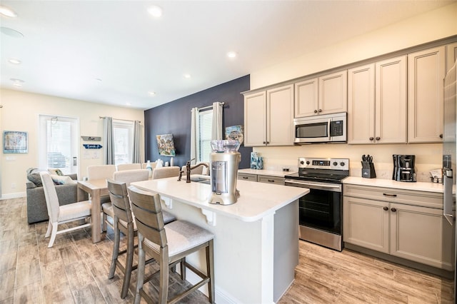 kitchen with appliances with stainless steel finishes, light wood-type flooring, sink, a center island with sink, and a breakfast bar area