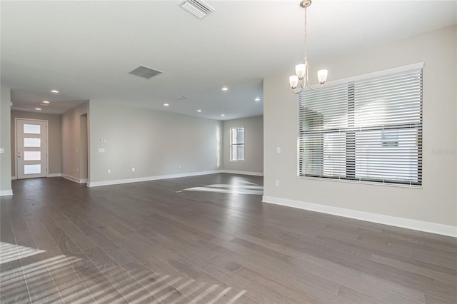 spare room featuring dark wood-style floors, visible vents, a notable chandelier, and baseboards