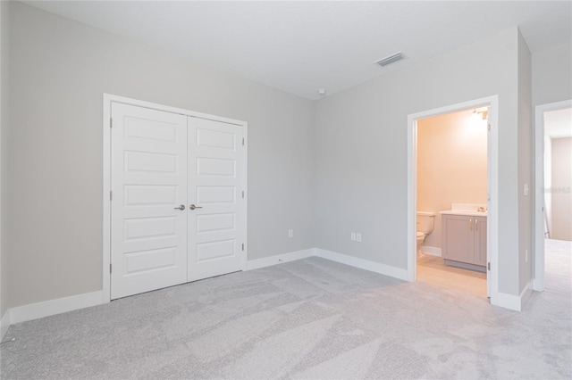 unfurnished bedroom with a closet, light colored carpet, connected bathroom, and baseboards