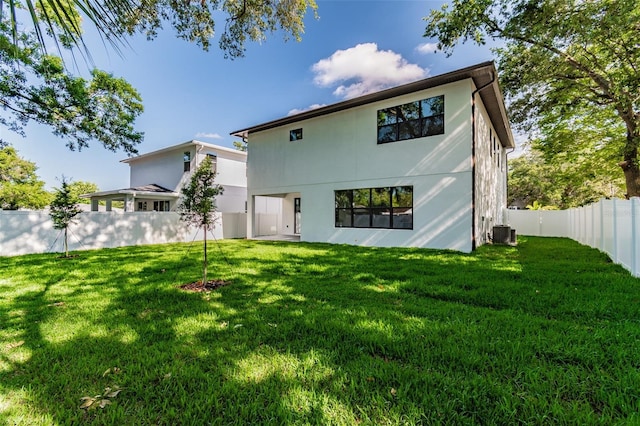 rear view of property with central AC unit, a lawn, a fenced backyard, and stucco siding