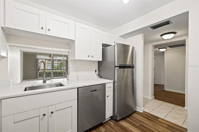 kitchen featuring white cabinets, sink, light stone countertops, light wood-type flooring, and stainless steel appliances