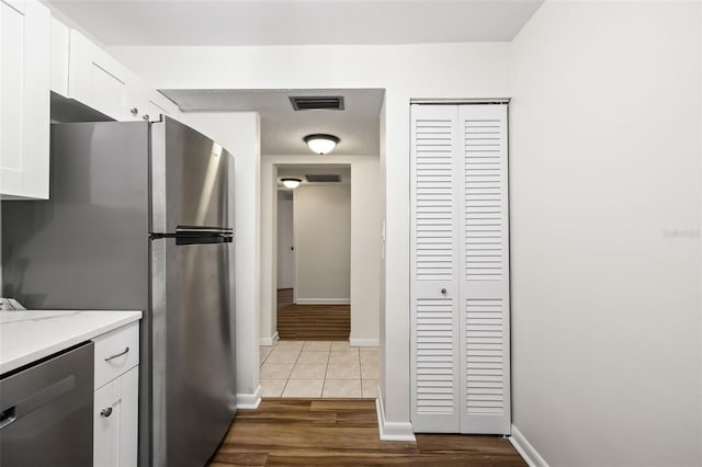 kitchen with light tile patterned floors, light stone counters, a textured ceiling, white cabinets, and appliances with stainless steel finishes