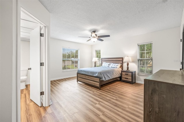 bedroom featuring a textured ceiling, ensuite bathroom, light hardwood / wood-style flooring, and ceiling fan