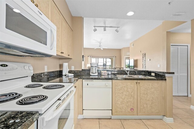 kitchen with kitchen peninsula, dark stone counters, track lighting, white appliances, and light tile patterned floors