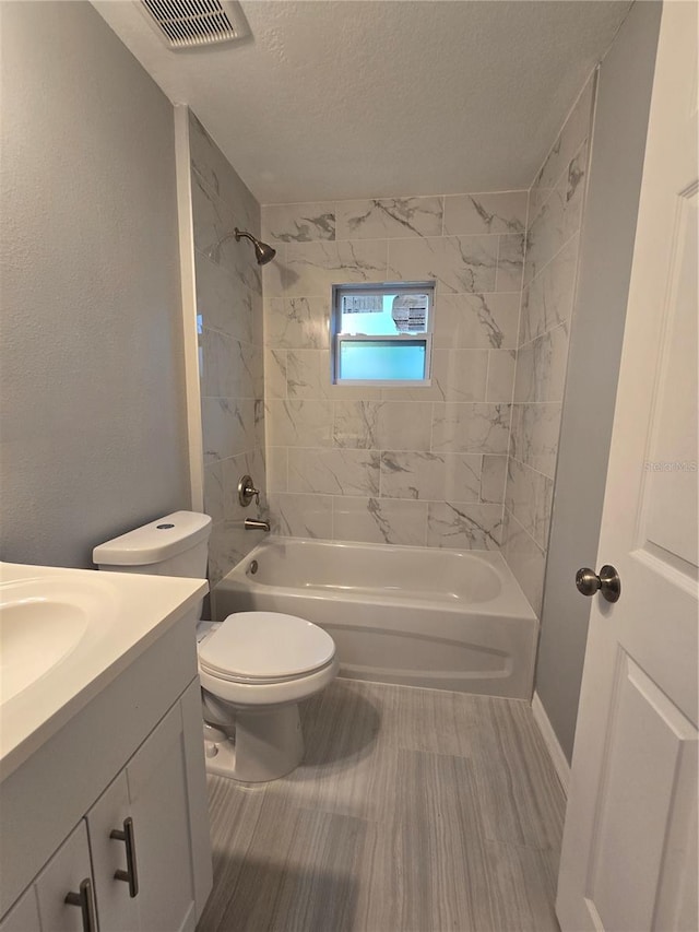 full bathroom with tiled shower / bath, vanity, a textured ceiling, and toilet