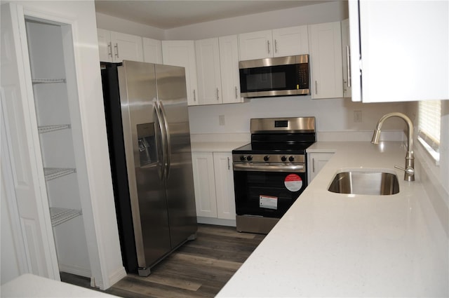 kitchen with white cabinets, stainless steel appliances, a sink, light countertops, and dark wood-type flooring