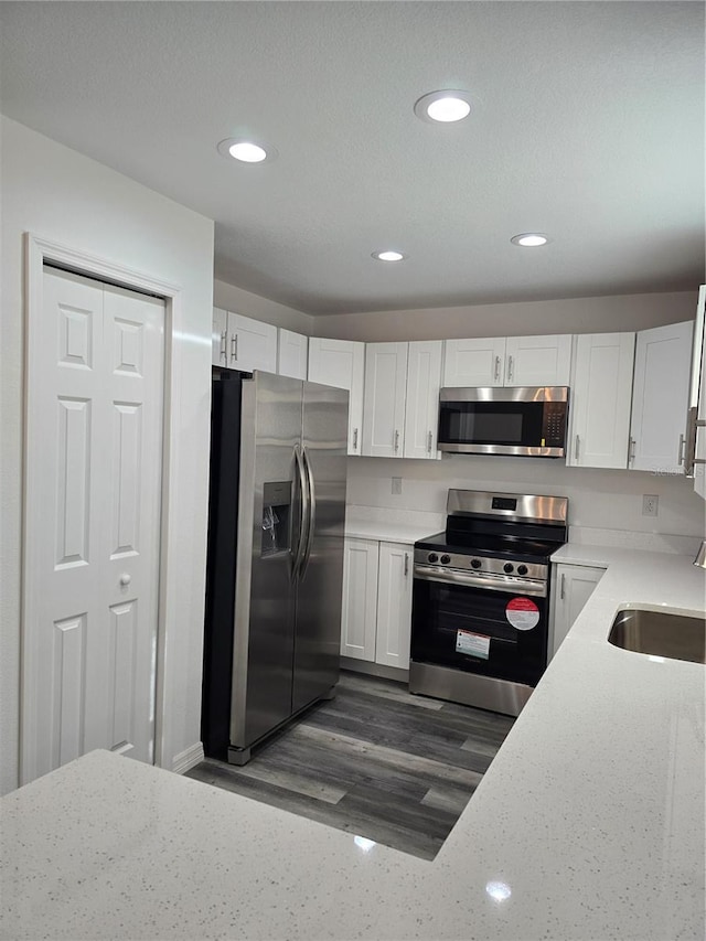 kitchen with white cabinets, stainless steel appliances, light stone countertops, and a sink