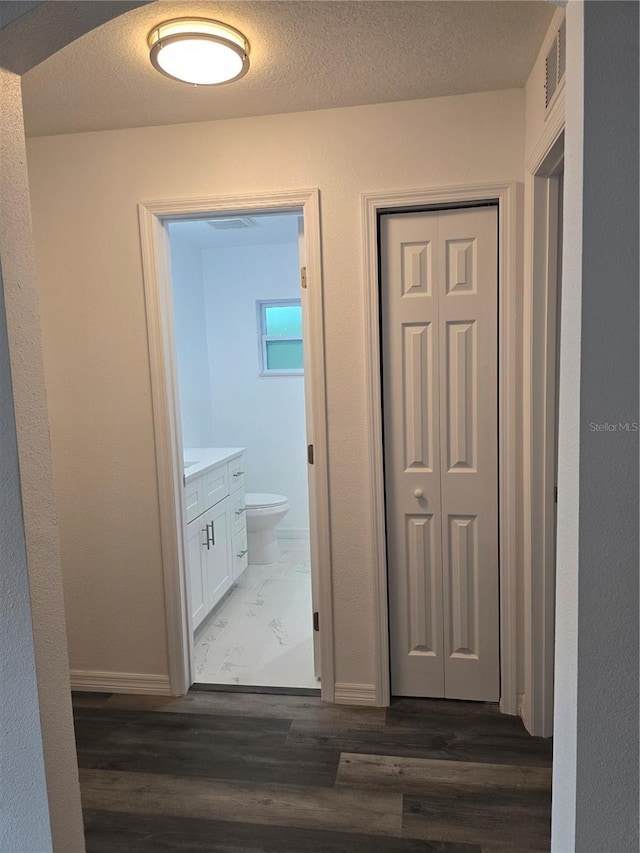 corridor with visible vents, baseboards, and dark wood-style flooring