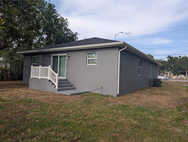 rear view of property featuring stucco siding, a yard, and central AC