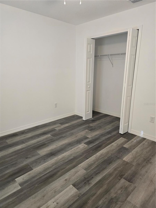 unfurnished bedroom featuring dark wood finished floors, a closet, baseboards, and visible vents