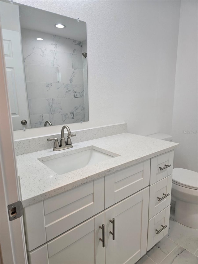 bathroom featuring toilet, marble finish floor, vanity, and a tile shower