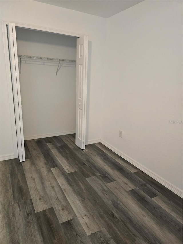 unfurnished bedroom with dark wood finished floors, baseboards, and a closet