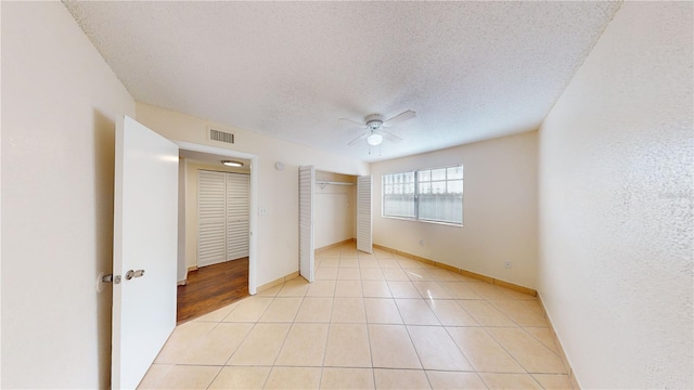 unfurnished bedroom featuring ceiling fan, a closet, a textured ceiling, and light tile patterned floors